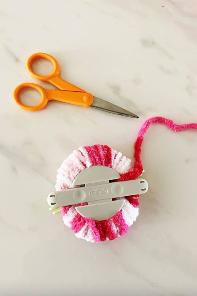 Once the yarn has been wrapped around the clover pom pom maker you're ready to cut it. WildflowersAndWanderlust.com